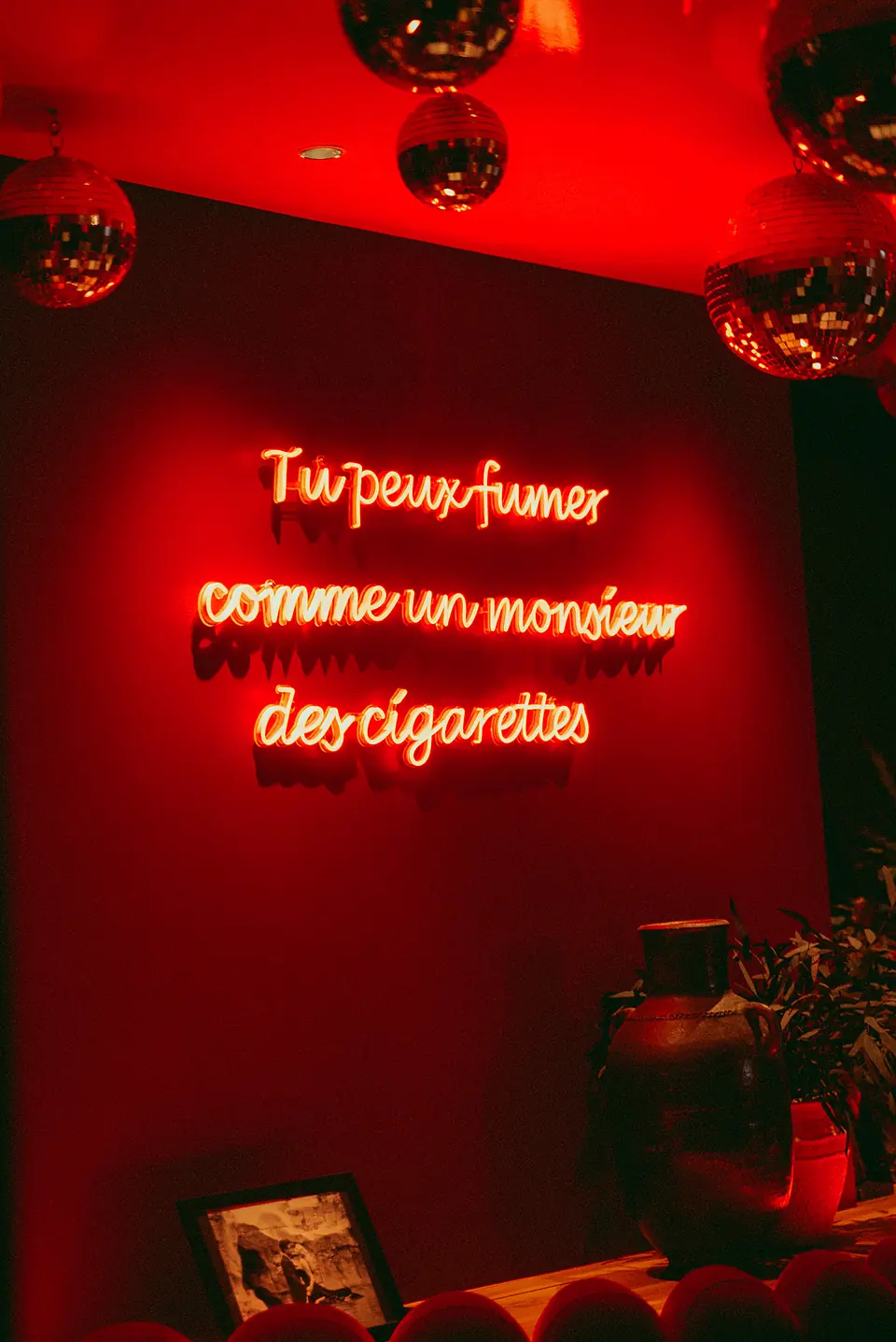 Le néon « Tu peux fumer comme un monsieur des cigarettes » sur le mur rouge